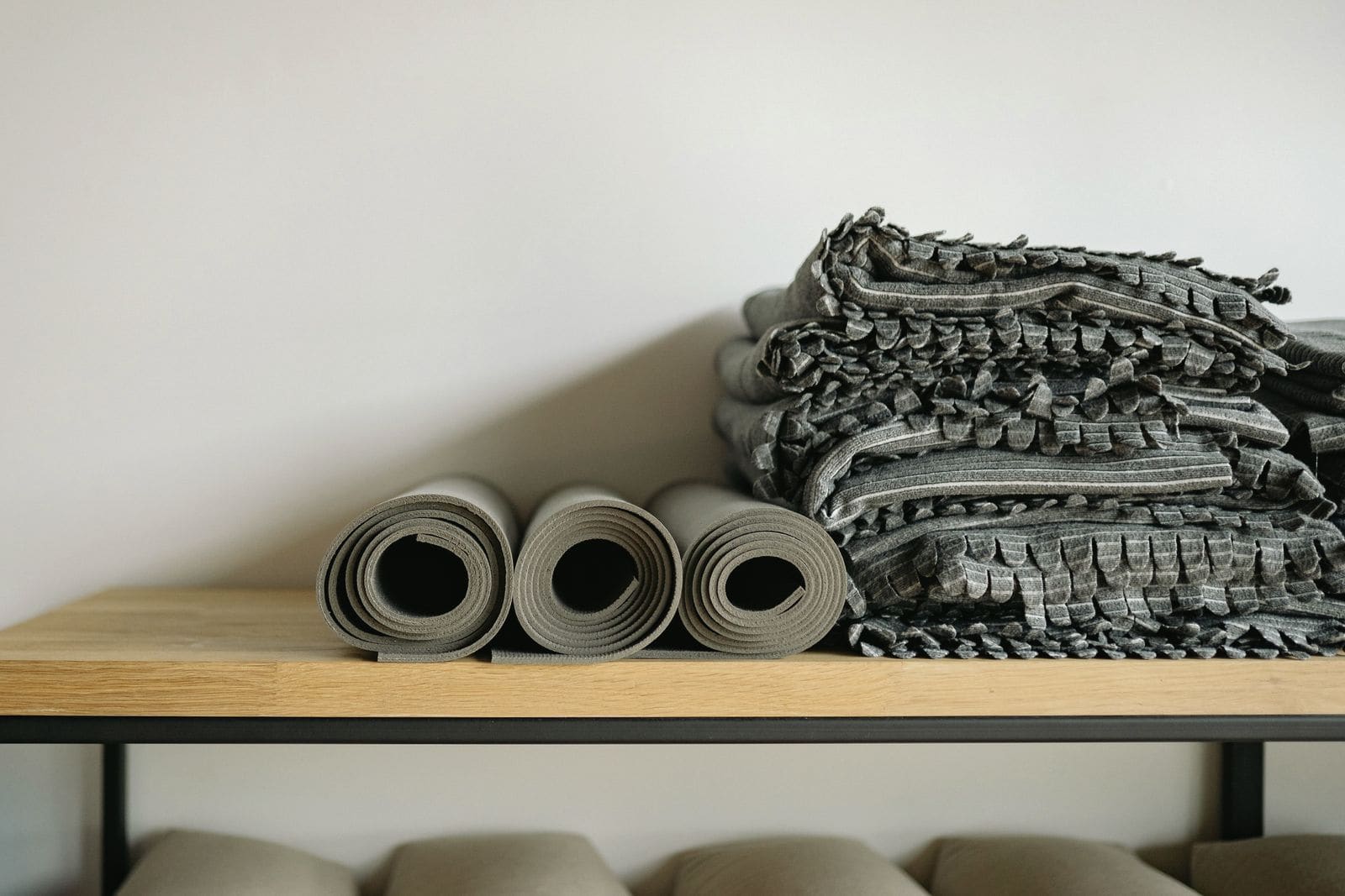 Rolled yoga mats and folded blankets on an oak bench, with bolsters resting beneath